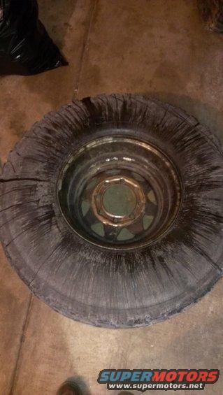 Worn tire on a metal rim, with a black trash bag in the background