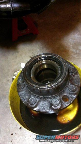Wheel hub assembly with bolts submerged in dark oil within a yellow bucket