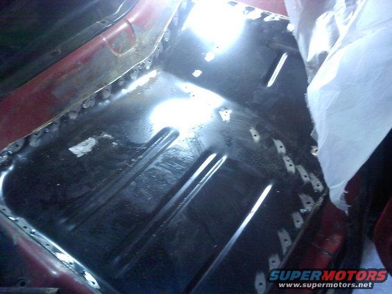 Close-up of a vehicle's floor pan undergoing repair with visible welds and a new metal patch