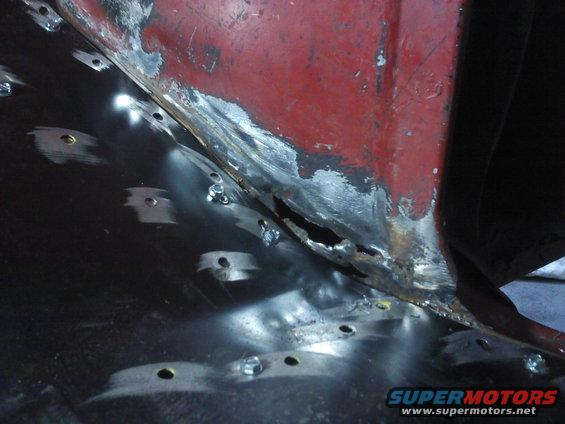 Close-up of a rusted-out vehicle floor pan being repaired with new metal and bolts