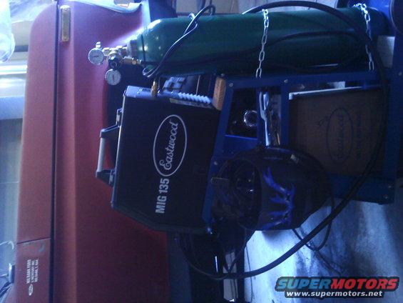 Welding machine and gas tank on a cart next to a red vehicle door
