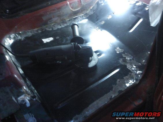 Grinding tool on rusty vehicle floor pan, red interior visible