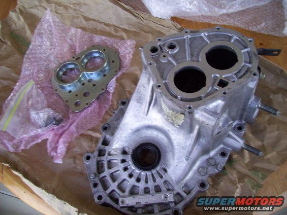 Transmission housing and adapter plate laid out on brown paper. Some small parts are in a plastic bag