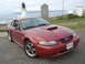 2003 Mercury Marauder - A red Ford Mustang is parked by the coast with a lighthouse and a monument in the background.