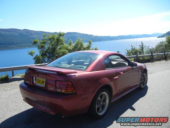 Red coupe with a spoiler, GT badge, and license plate T23 LBP parked by a lake