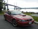 2003 Mercury Marauder - This red Ford Mustang coupe, likely a 2003 model, is seen parked near a large bridge and body of water.