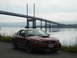 2003 Mercury Marauder - Red Ford Mustang coupe parked near a large bridge over water.