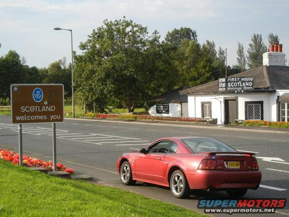 Red Ford Mustang GT parked by Scotland welcome sign