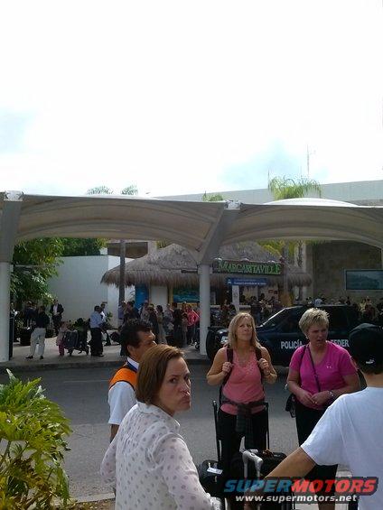 Black police SUV with "POLICIA" text, parked near an entrance with people and luggage