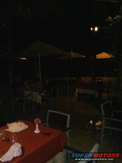 Outdoor dining tables with red tablecloths and chairs at night, some with umbrellas overhead