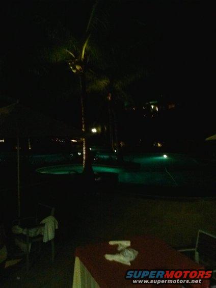 Swimming pool and palm trees at night with tables and chairs in the foreground