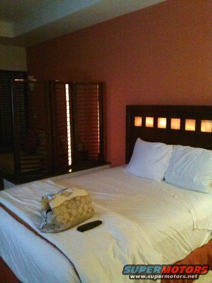 Hotel room with a made bed, pillows, a purse, and a remote control