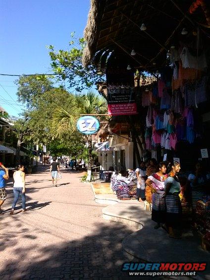 Street scene in a tropical location with shops selling clothing and textiles, people walking and browsing