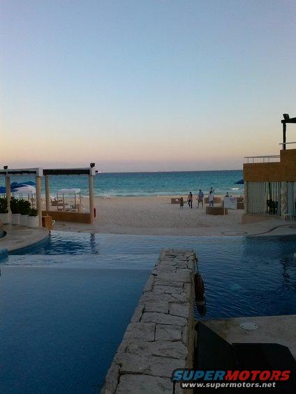 Infinity pool overlooking a sandy beach and turquoise ocean at sunset