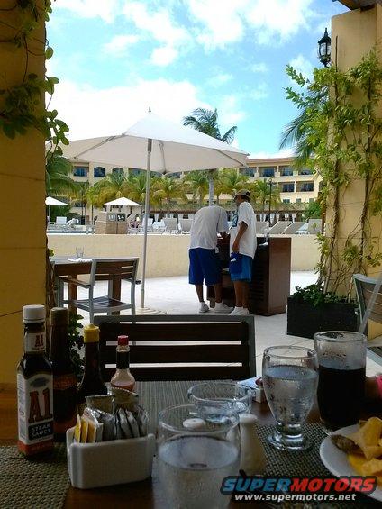 Table with A1 steak sauce bottles and drinks, with people standing by a pool in the background