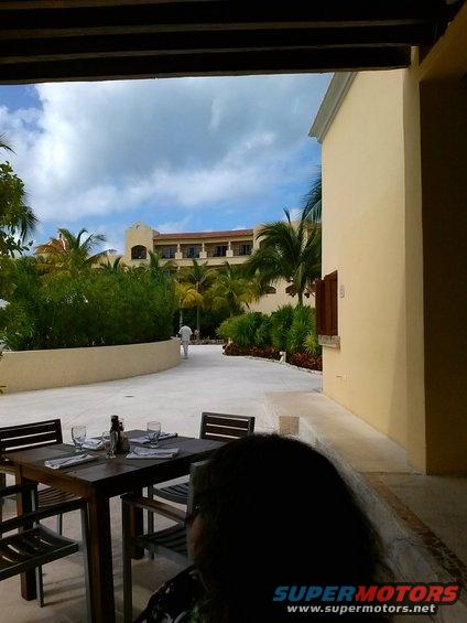 Outdoor dining table set for a meal, with a resort building and palm trees in the background