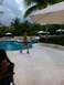 1960 Ford Falcon - A woman strolls past a swimming pool at a tropical resort, with lounge chairs and palm trees visible.