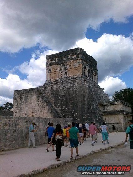 Tourists walk towards El Castillo pyramid under a cloudy sky