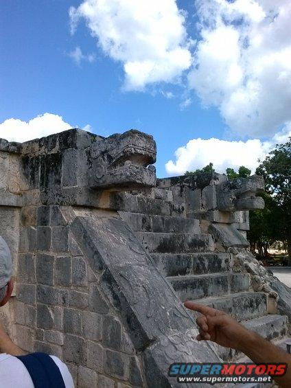 Stone serpent heads on ancient ruins with blue sky and clouds
