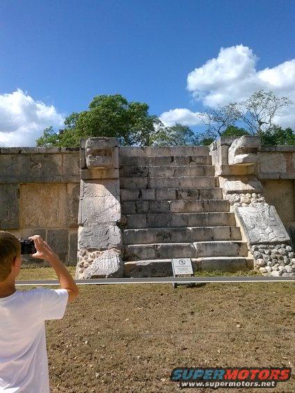 Person photographing ancient stone steps with serpent carvings under a blue sky