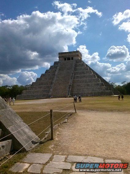 Pyramid at Chichen Itza with clouds in the sky. Some people are walking around