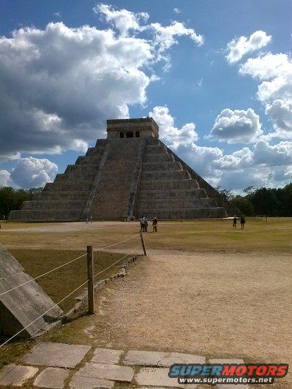 Mayan pyramid under a cloudy sky, with people walking on the grounds