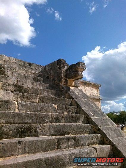 Stone serpent carving on ancient stairs under a blue sky with clouds