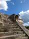 1960 Ford Falcon - A detailed stone carving of a serpent's head adorns the side of ancient stone steps, set against a backdrop of a bright blue sky with scatt…