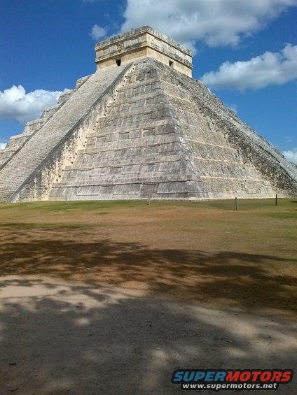 Stone pyramid with steps under a blue sky with clouds, grass in foreground