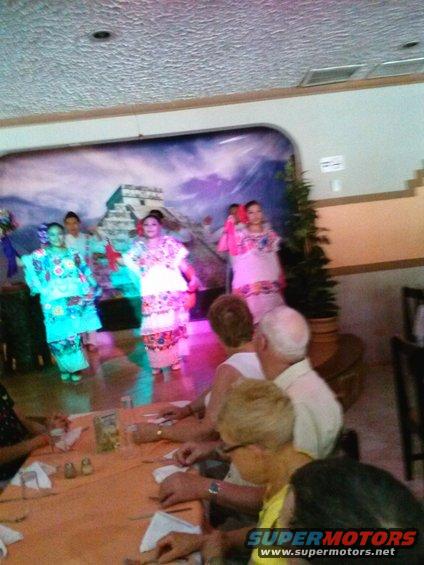 People watch a cultural dance performance on a stage with a Mayan pyramid backdrop