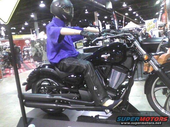Black motorcycle with a mannequin wearing a purple shirt and black leather pants, sitting on it. The mannequin has a black helmet