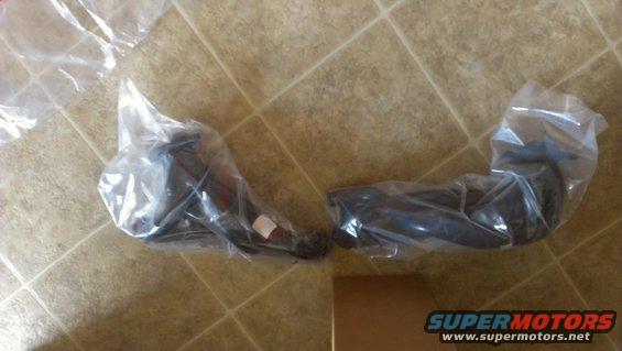 two new suspension parts in plastic wrap on a tiled floor