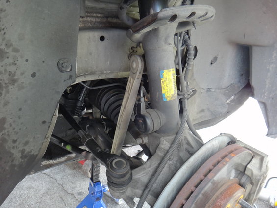 Car suspension with shock absorber, tie rod, and brake rotor. Yellow sticker on shock