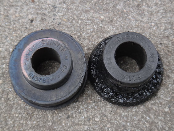 Two rubber suspension bushings on a concrete surface; one is dark gray with pinkish markings, the other is black and degraded
