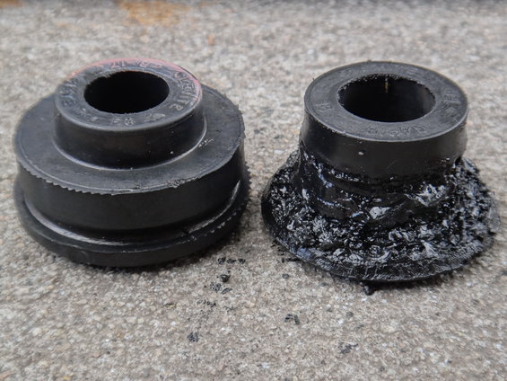Two black rubber suspension bushings on a concrete surface; one is intact, the other is degraded and melted