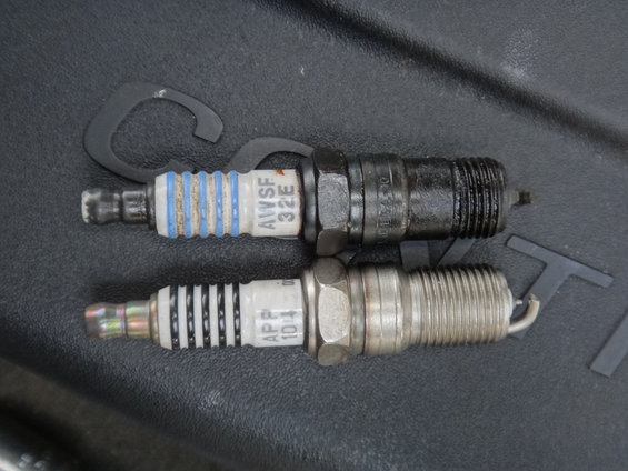 Two spark plugs, one with blue and white bands and text "AWSF 32E", the other with black and white bands and text "APF 10-4"
