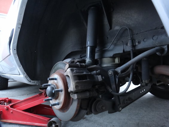 Rear suspension and brake assembly of a car, with a red jack supporting it