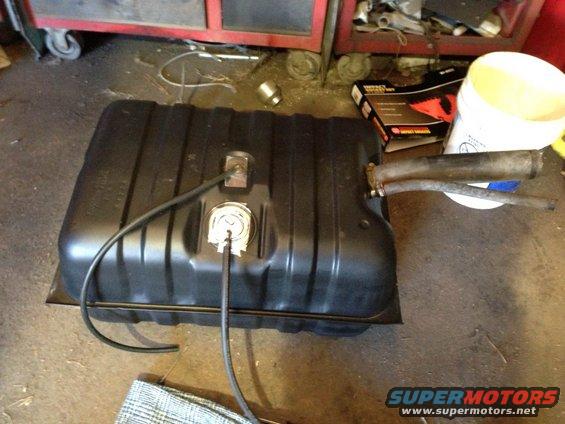 Black fuel tank with hoses and a sender unit, resting on a garage floor