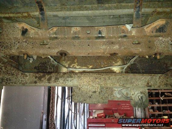 Heavily rusted vehicle frame and undercarriage components, with wiring visible