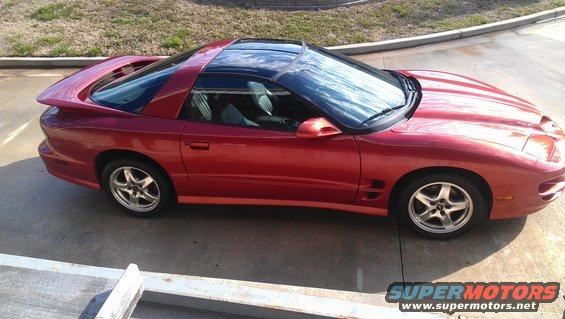 Red coupe with black t-top roof, side view. Looks like a late 90s Pontiac Firebird