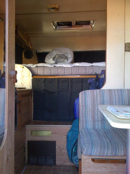 Interior view of a camper van showing a bed, bench seat, and table