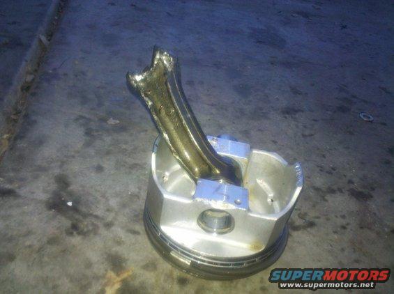 Broken engine piston with connecting rod sticking out of it, sitting on concrete