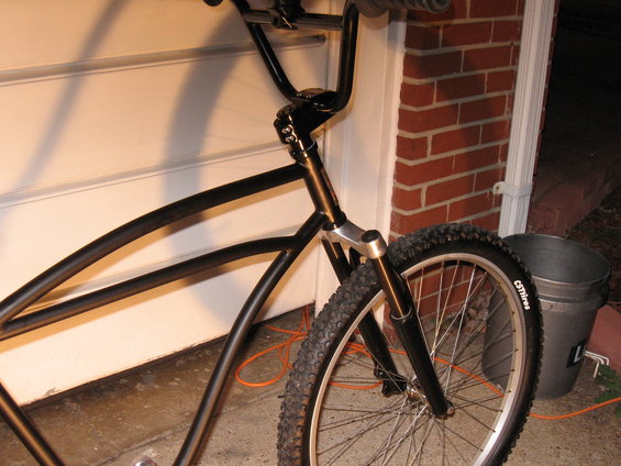 Black bicycle frame, handlebars, and front wheel with knobby tire. Bucket and brick wall in background