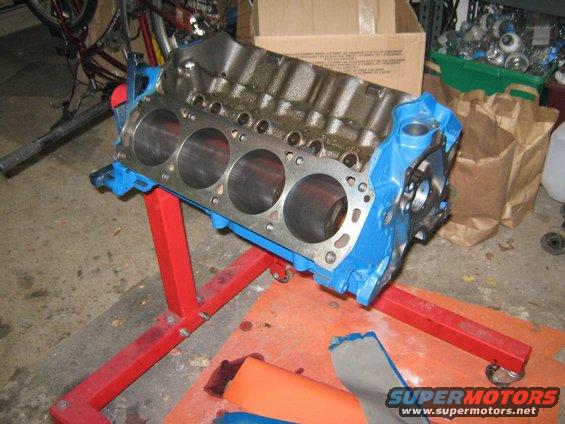 Engine block on a red stand, with cylinders visible. Background shows garage items