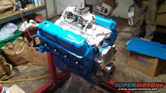 Blue V8 engine on a red stand, with carburetor and intake manifold visible