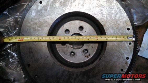 Metal flywheel with a yellow tape measure across it, showing approximately 12 inches