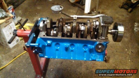 Blue Ford V8 engine block with crankshaft and pistons, mounted on a red engine stand