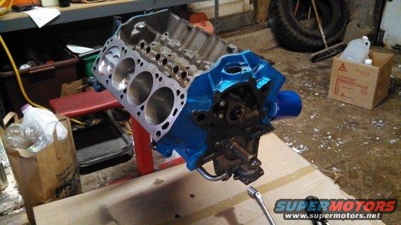 Blue painted V8 engine block on a red stand, with a wrench nearby