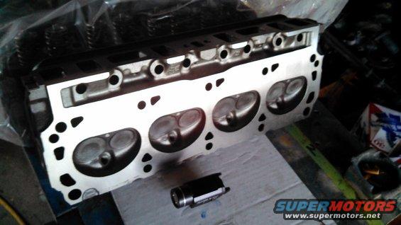 Engine cylinder head with four intake and exhaust ports visible, resting on a cardboard surface