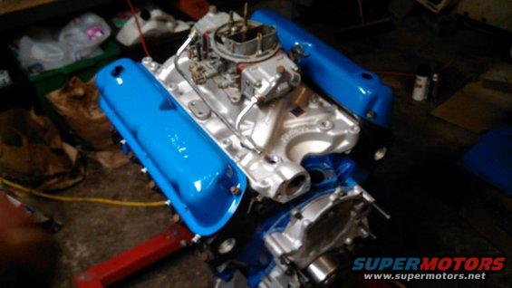 V8 engine with blue valve covers and a carburetor, on a red engine stand